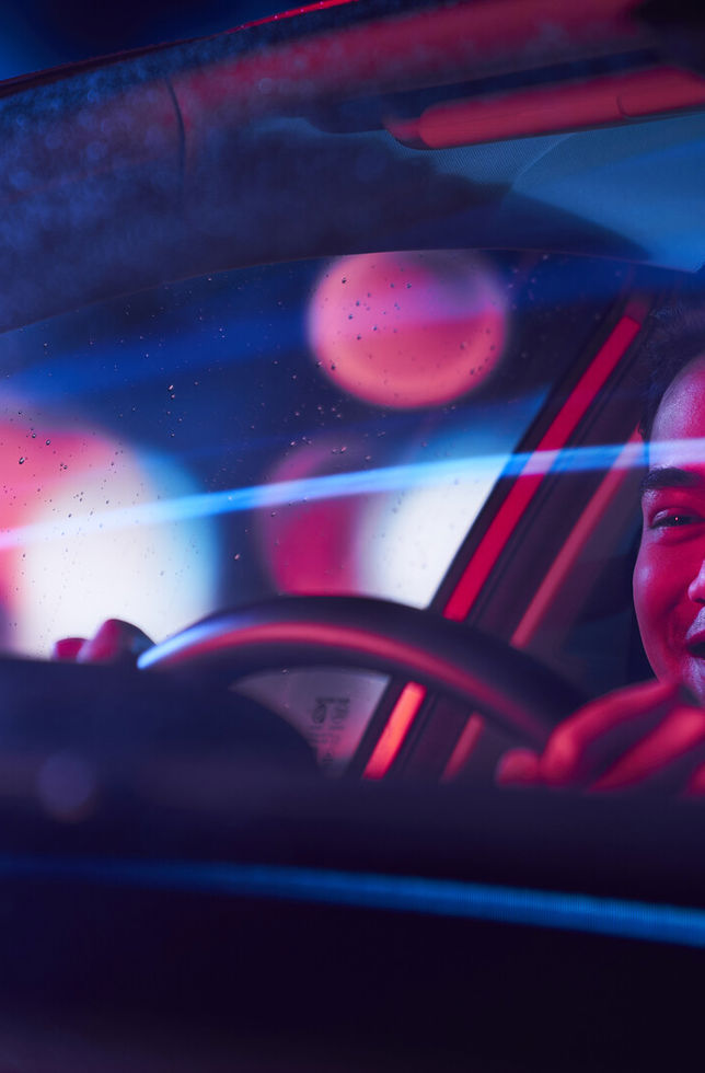 A smiling young man driving an electric car at night