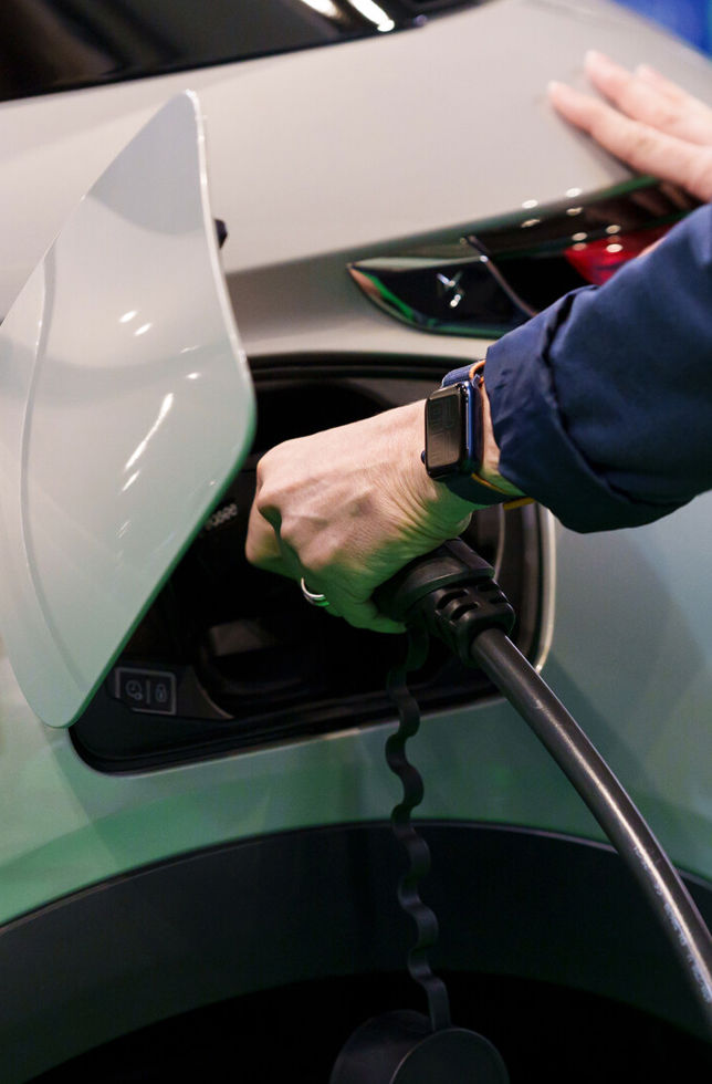 A close-up of a hand plugging a charging socket into an electric car
