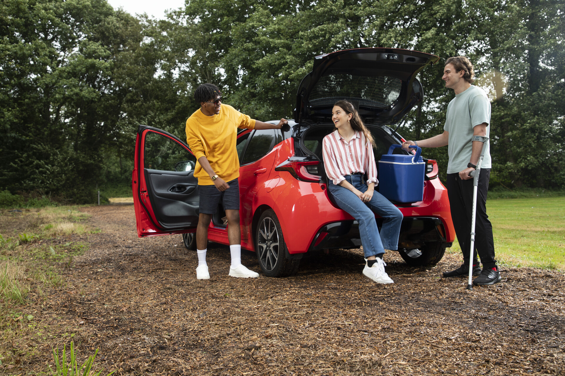 Three young people sit in and around the back of a car, smiling and talking