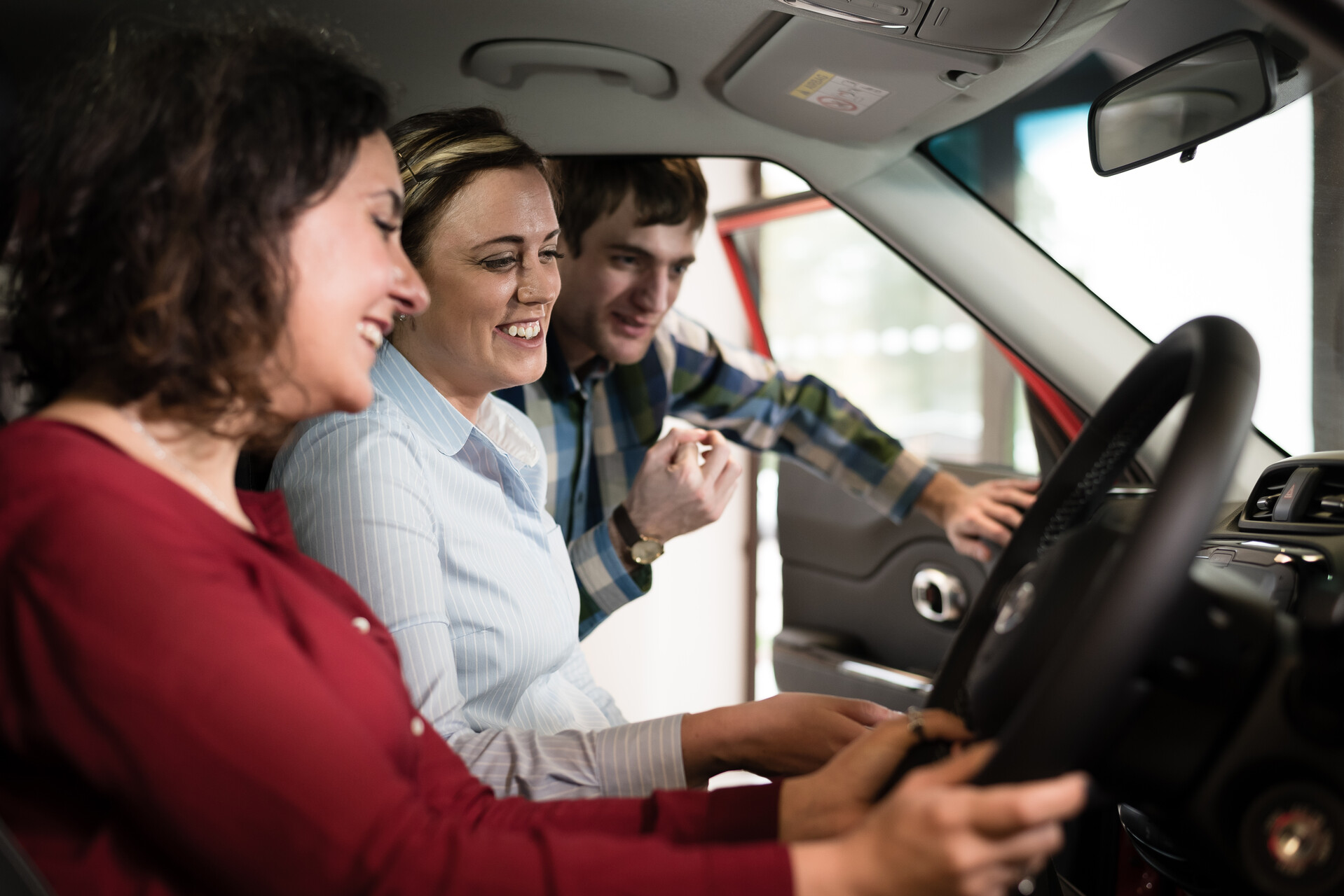 A dealer shows the inside of a car to a smiling woman and man