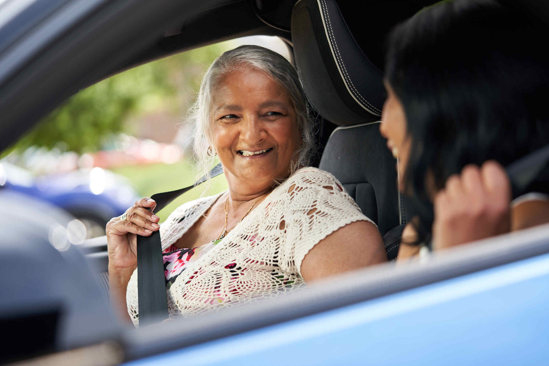 An older woman smiling and talking to a younger woman, inside a car