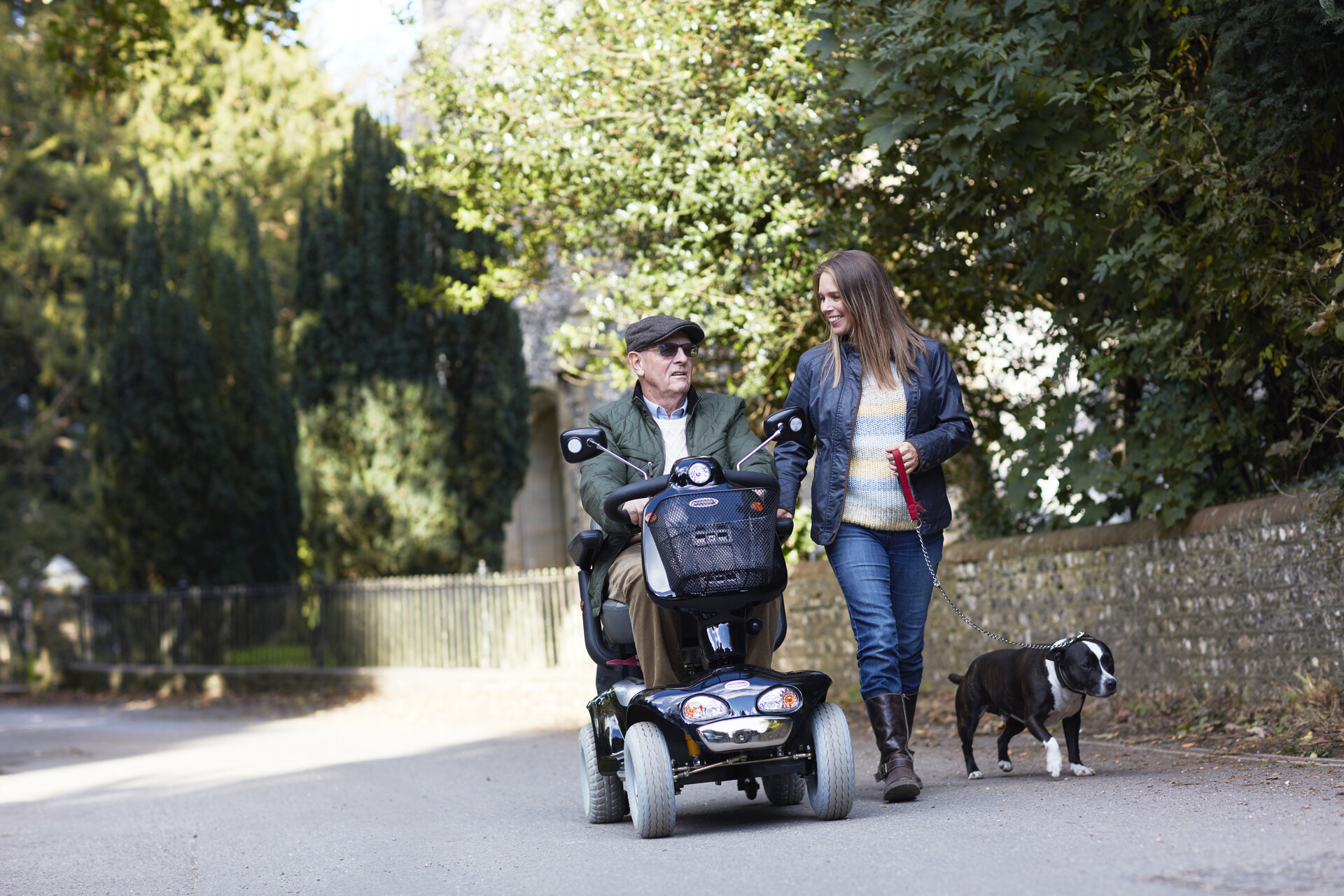 An older man riding a mobility scooter, next to a woman walking a dog