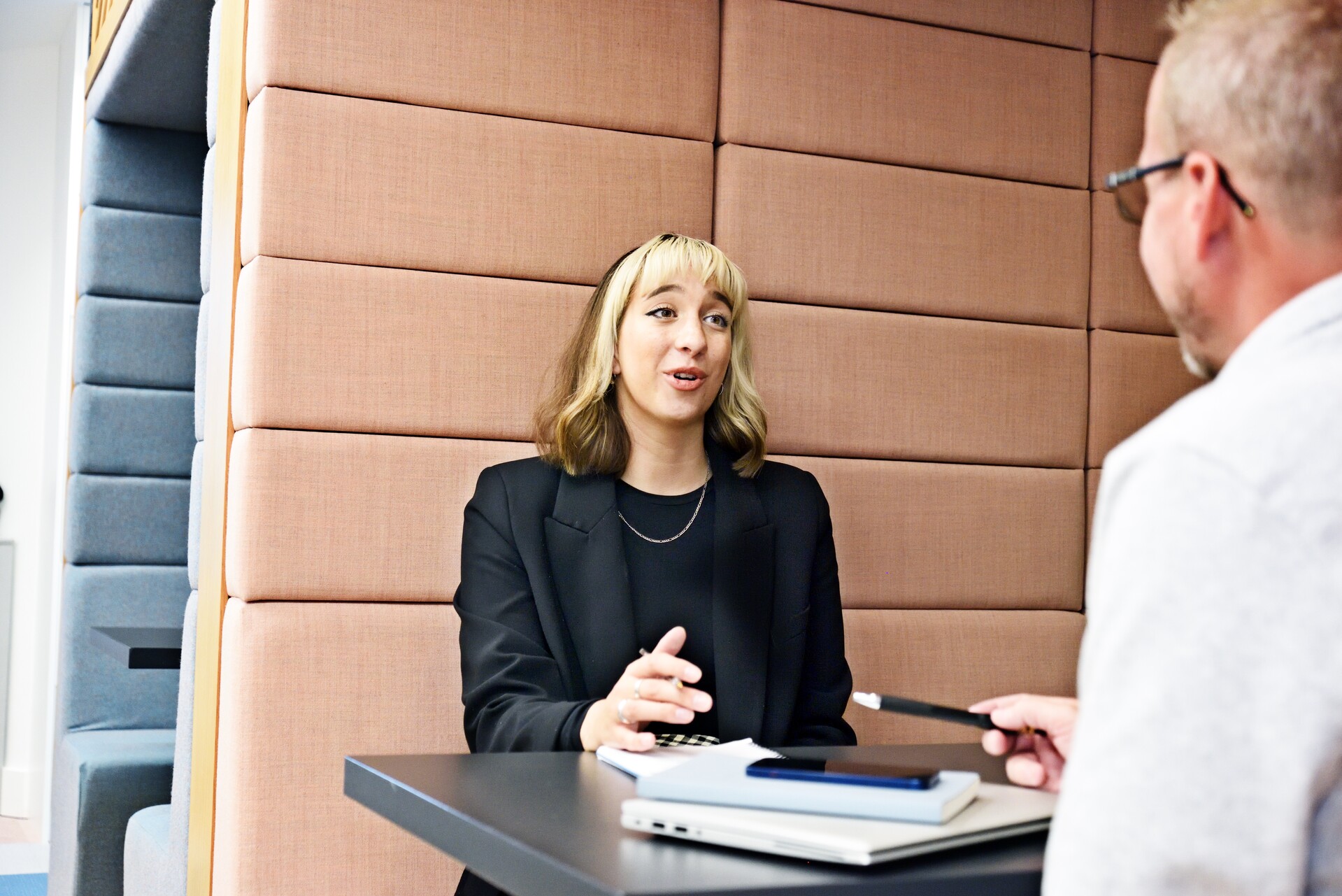A young woman talks to a man in an office booth