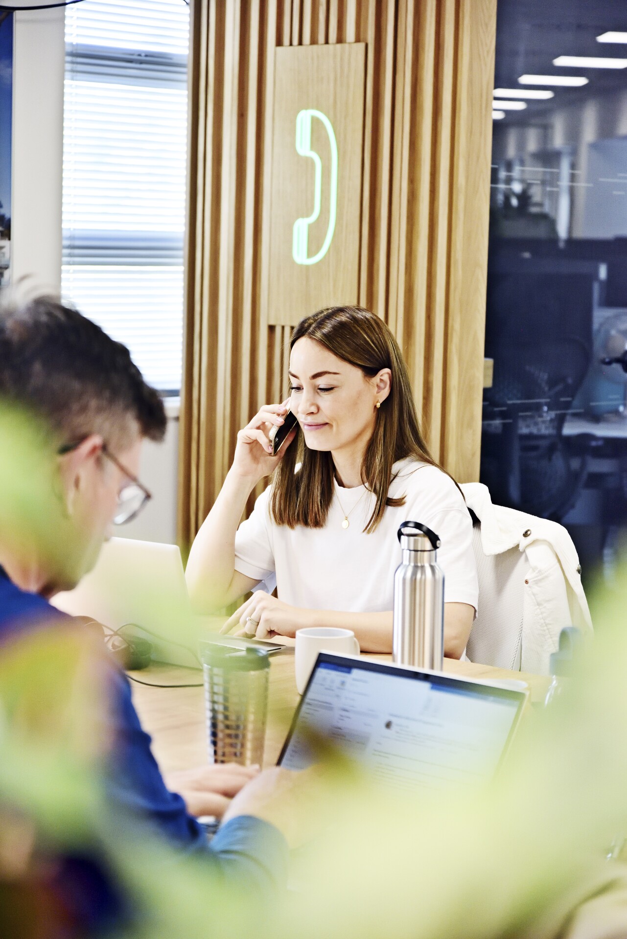 A woman uses a mobile phone in an office, while working on her laptop
