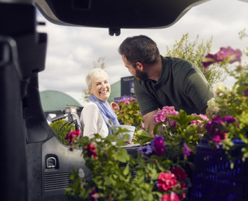 An older woman smiling and talking to a younger man, while he loads flowers into his boot