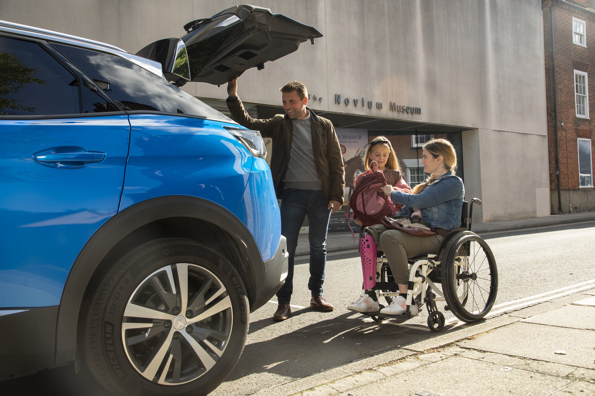 Man helping a woman in a wheelchair and a young girl unpack a car boot