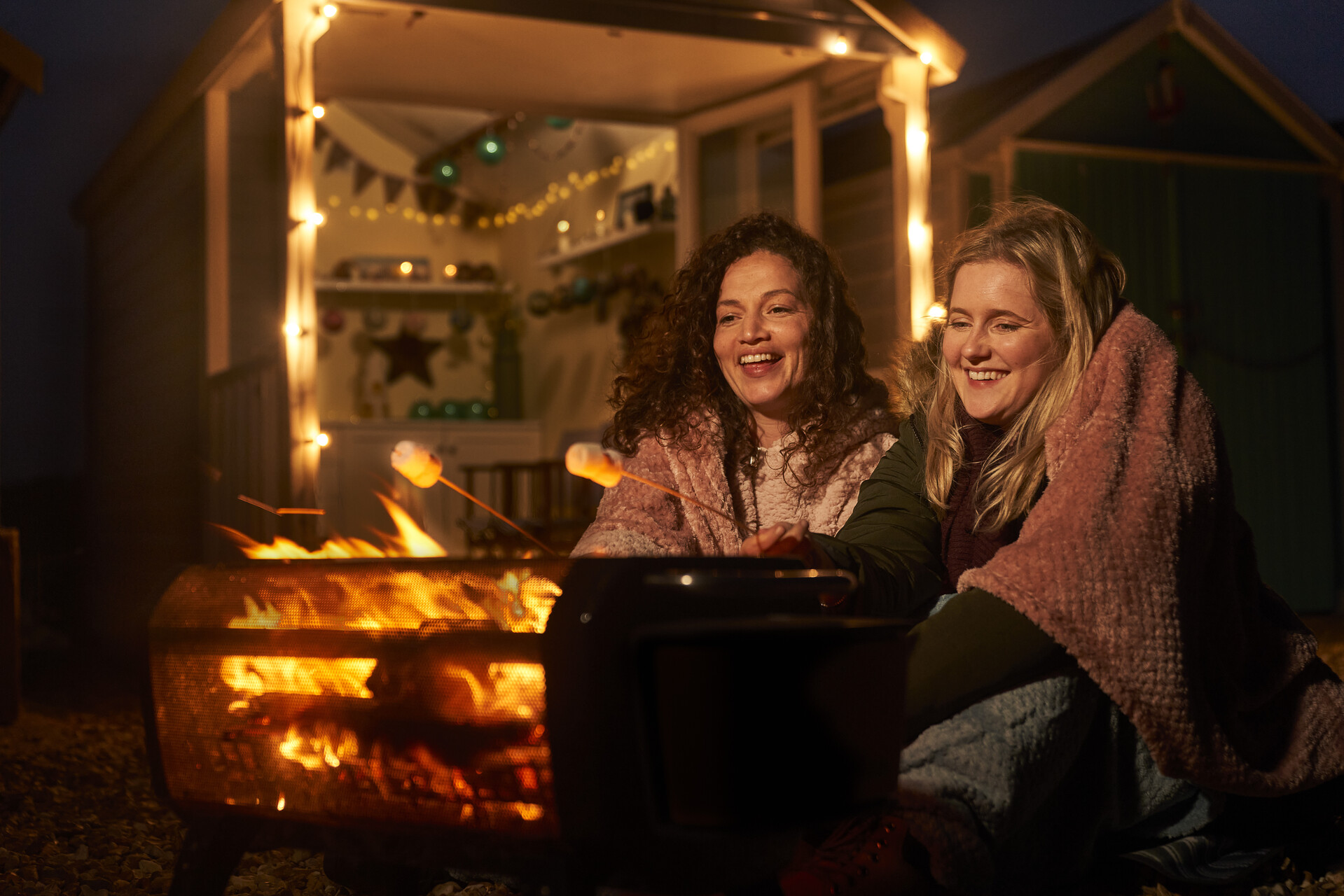 Two women roast marshmallows over a fire at night