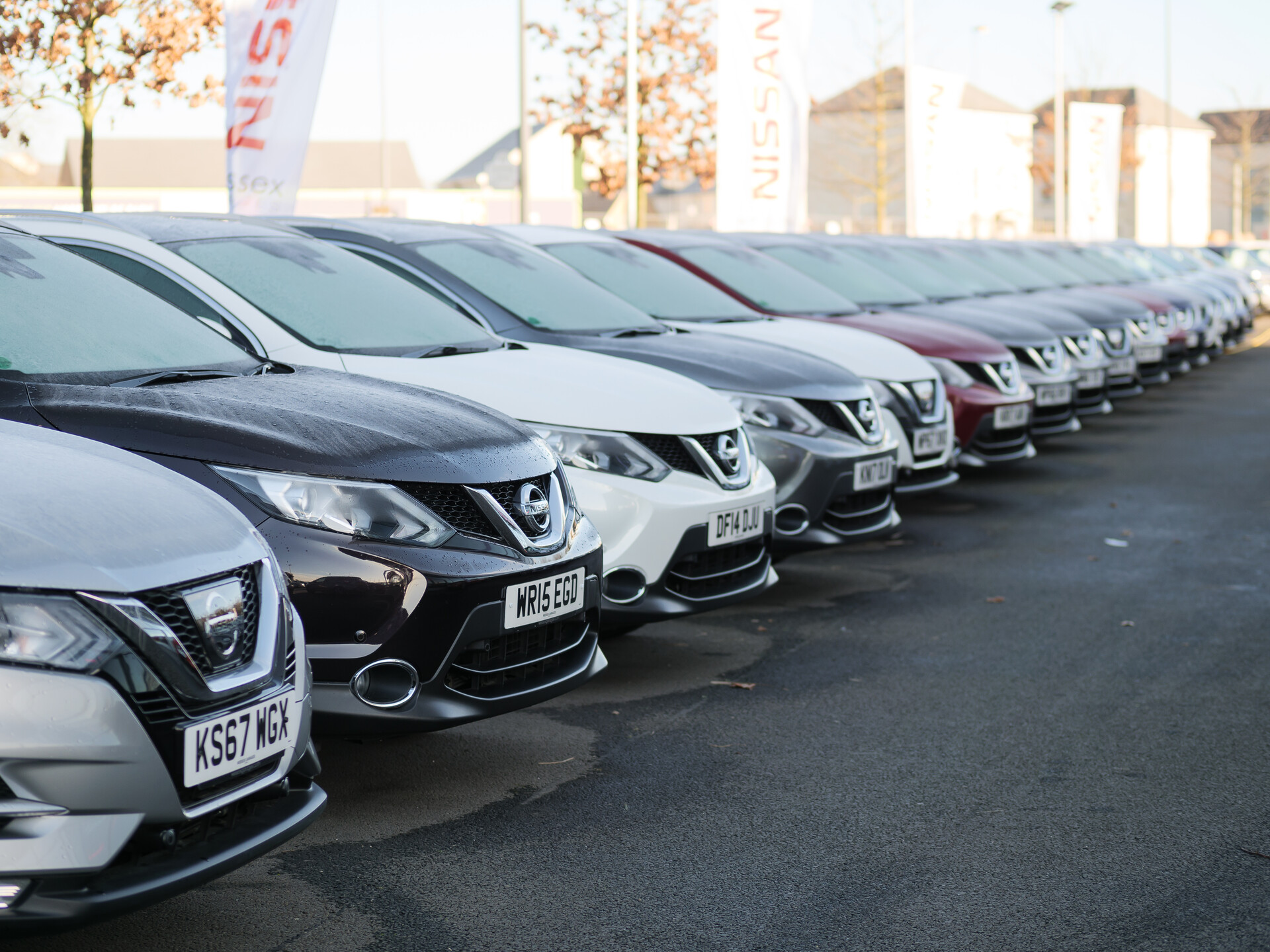 A close-up of a long row of Nissan cars, at a dealership