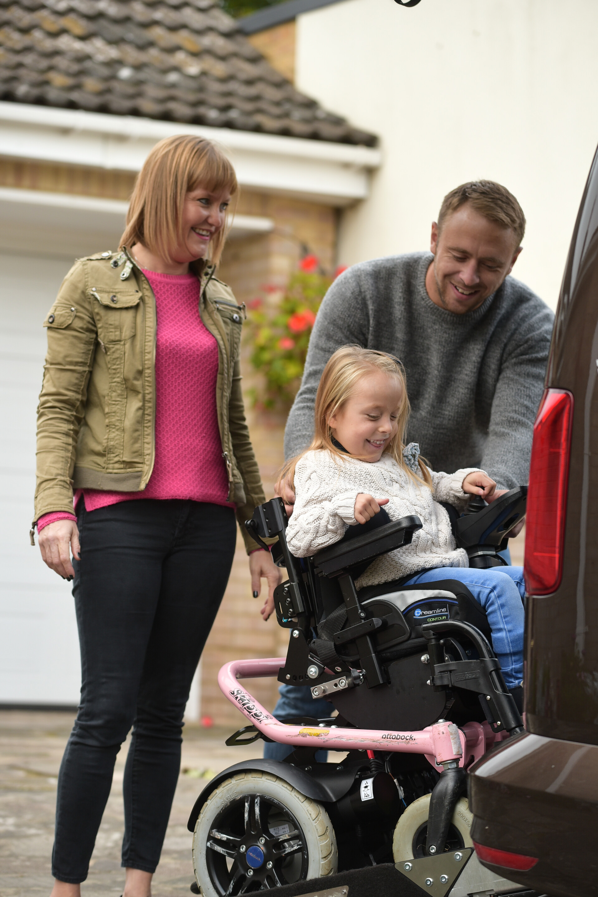 A man and woman smiling while helping a young girl in a wheelchair