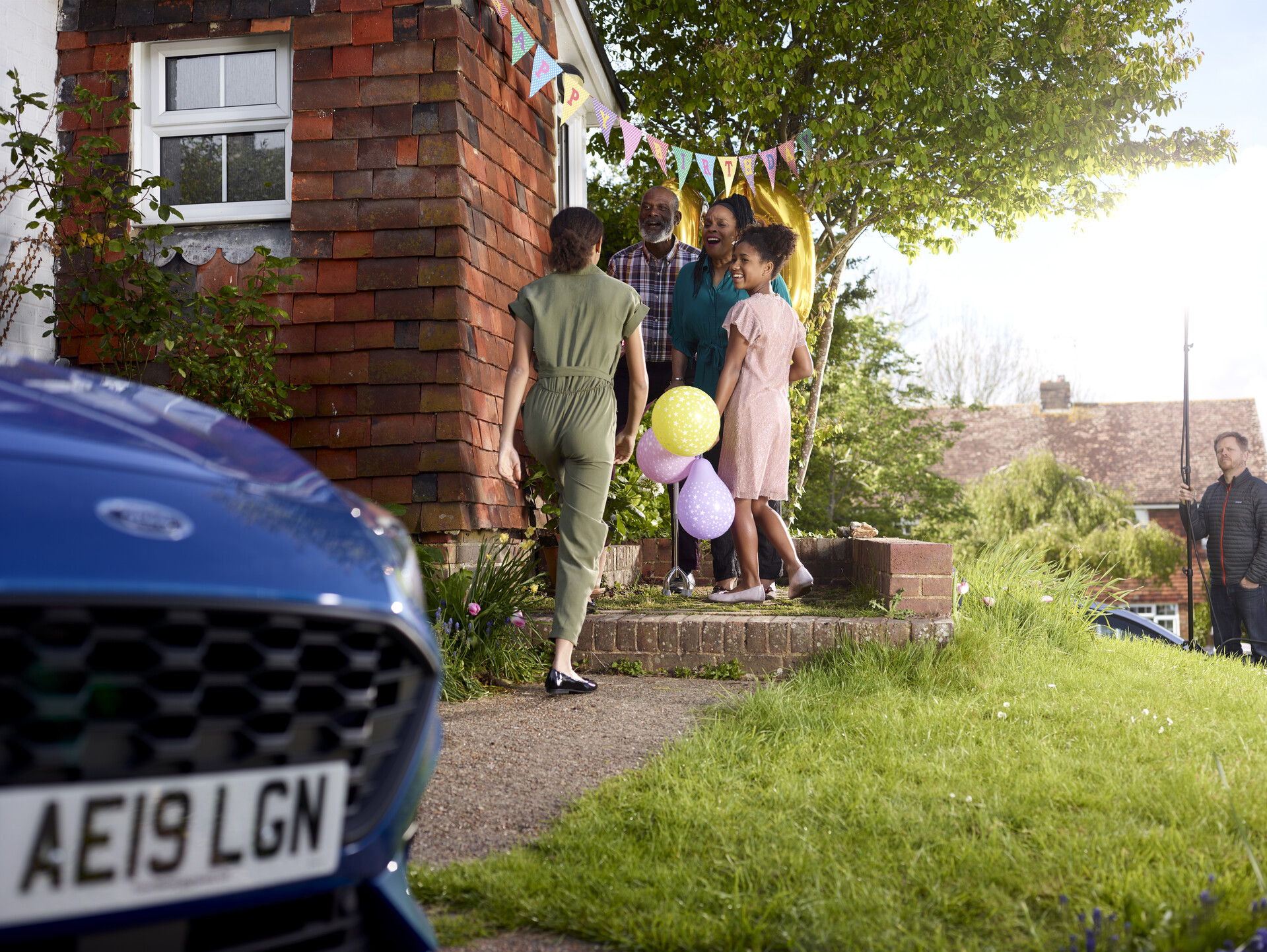 A woman is greeted as she arrives at a party, on the doorstop of a house with balloons