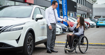 A dealer hands car keys to a woman in a wheelchair, next to her new car