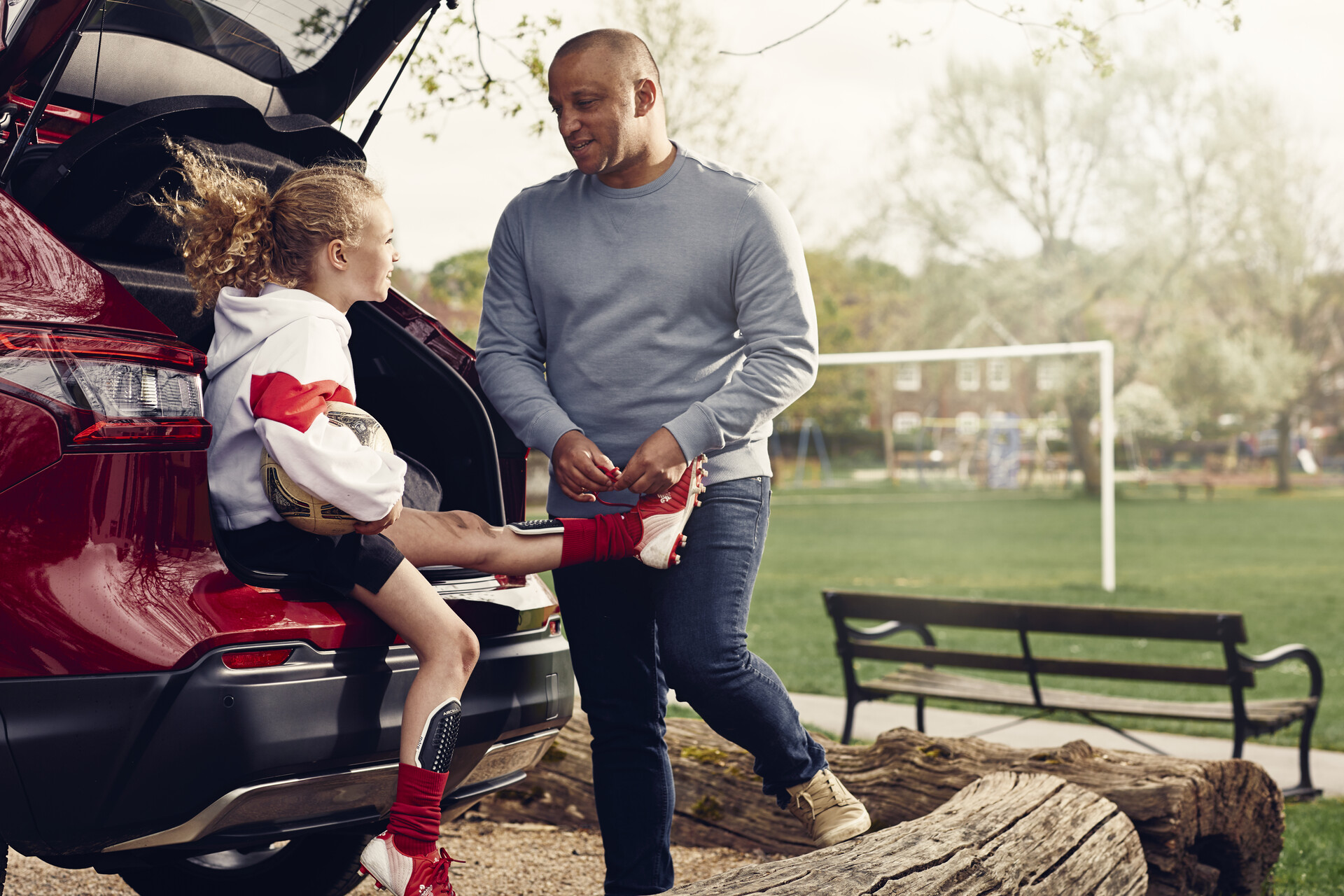 A man ties his daughter's sports shoe in the boot of a Motability Scheme hatchback car