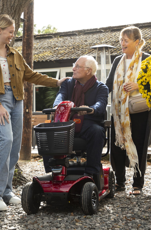 An older man on a mobility scooter looking and talking to a girl and a woman