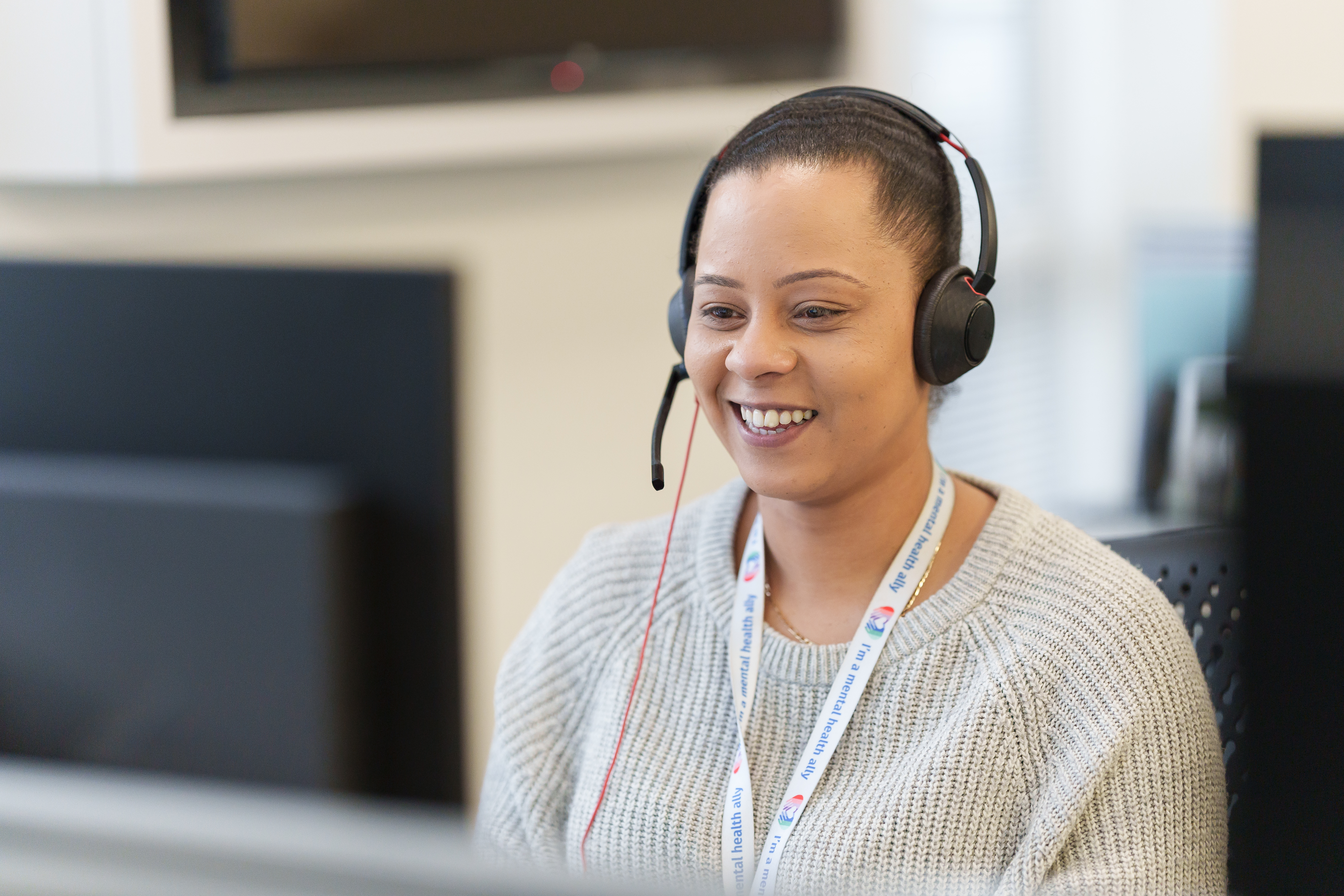 A smiling woman talking on a headset, in an office