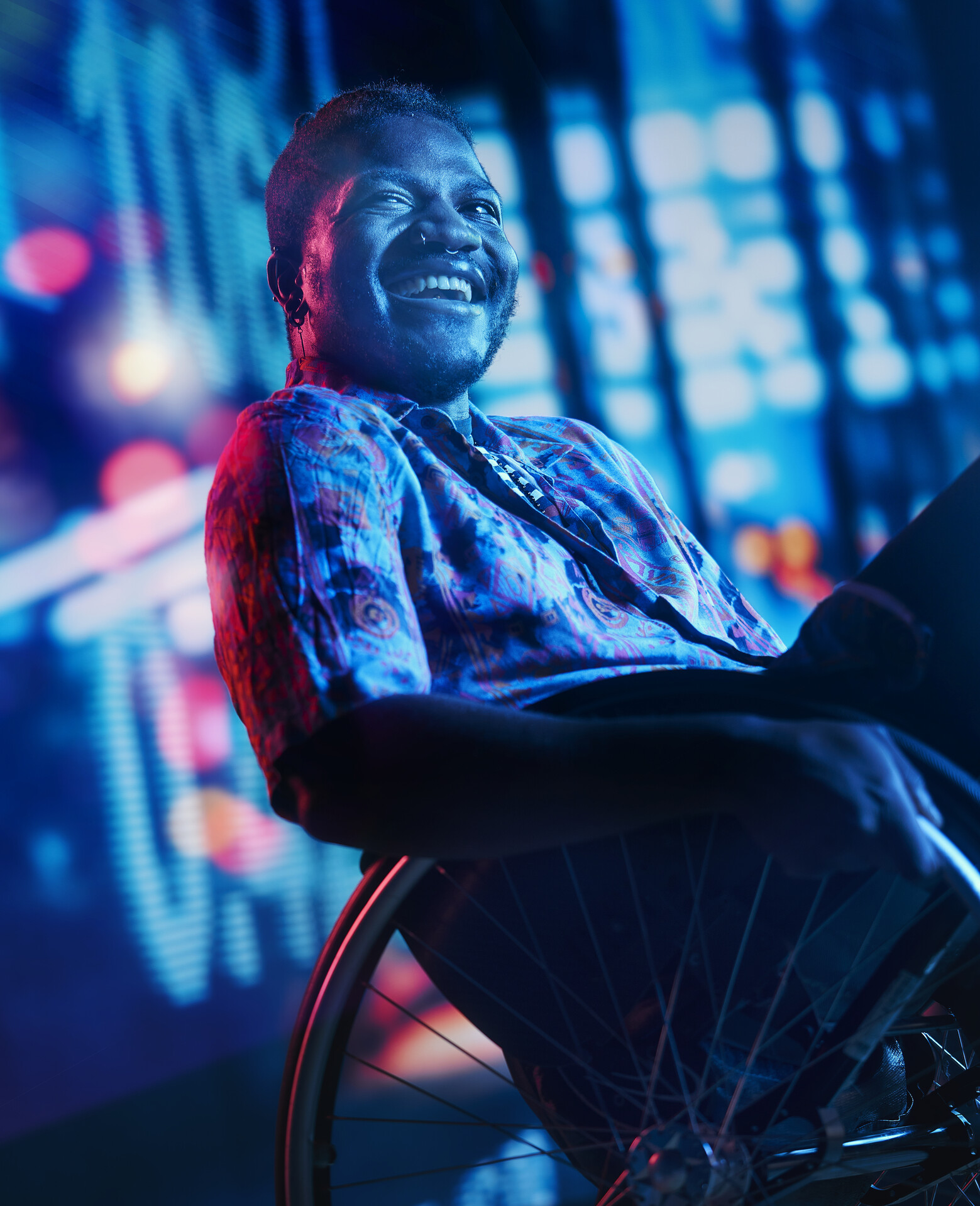 A man in a wheelchair laughing, in front of an digital screen