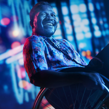 A man in a wheelchair laughing, in front of an digital screen