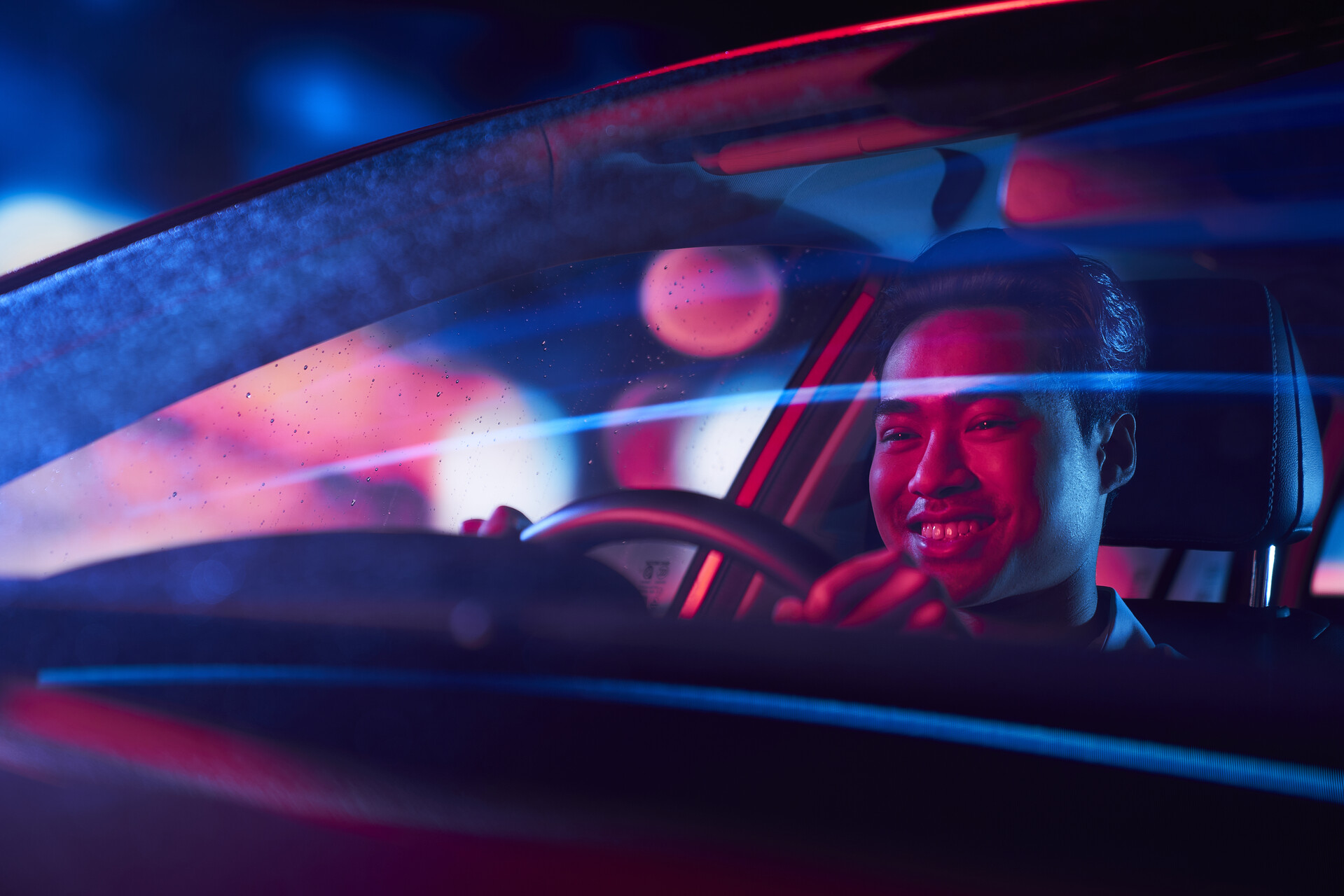 A smiling young man driving an electric car at night