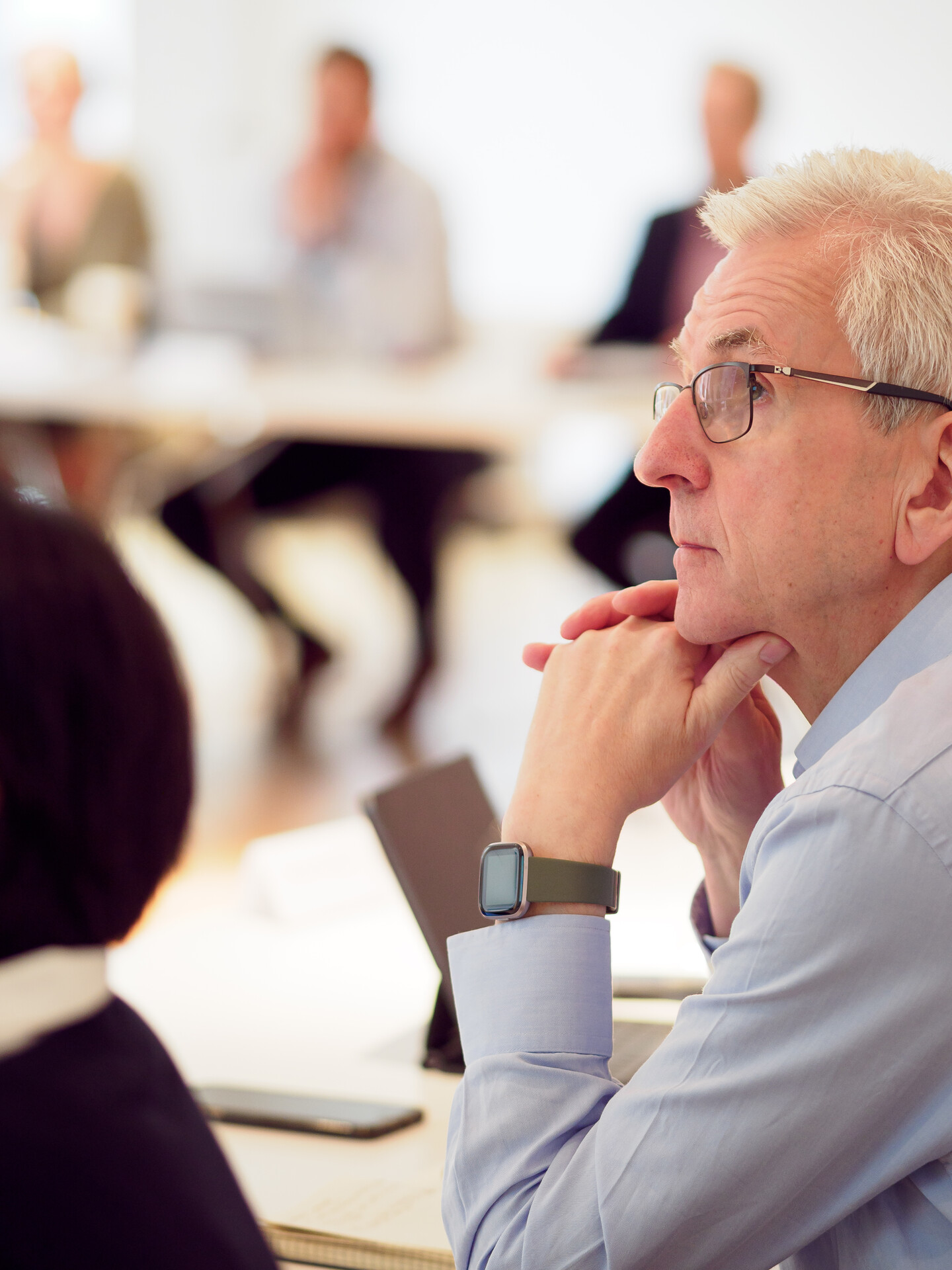 A close-up of an older man with glasses and a watch, watching a presentation