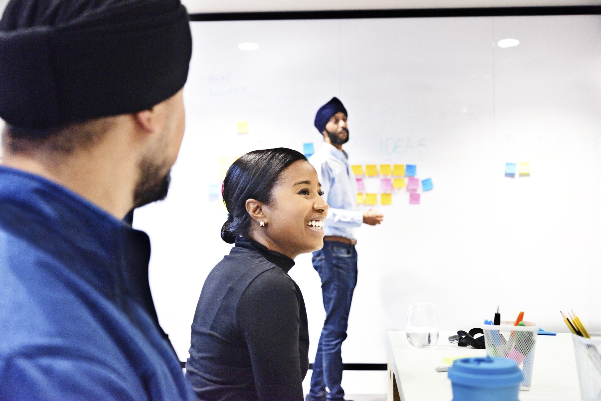A woman and two men in an office, with post it notes on a whiteboard