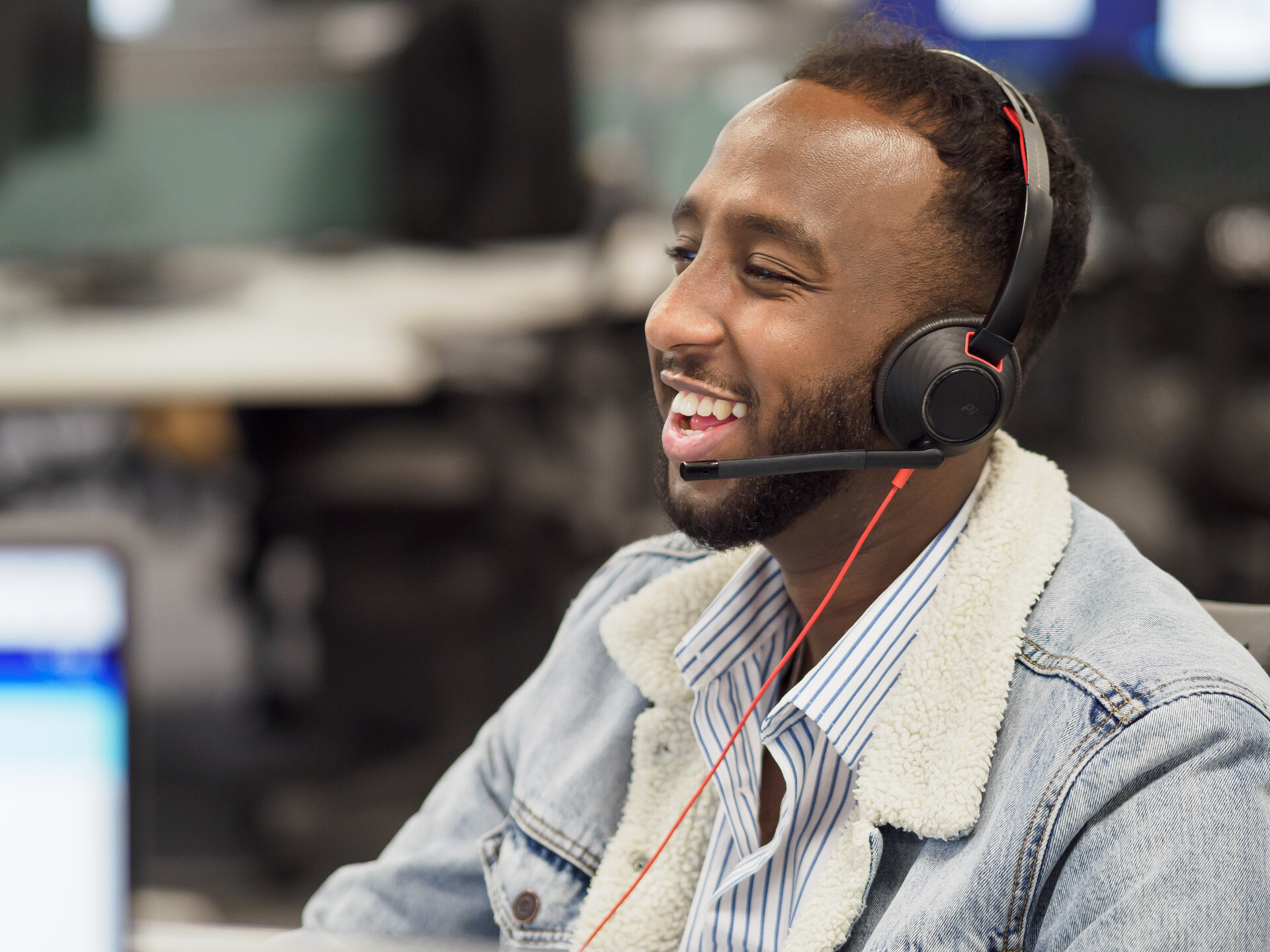 A man laughing while he talks on a headset, in an office