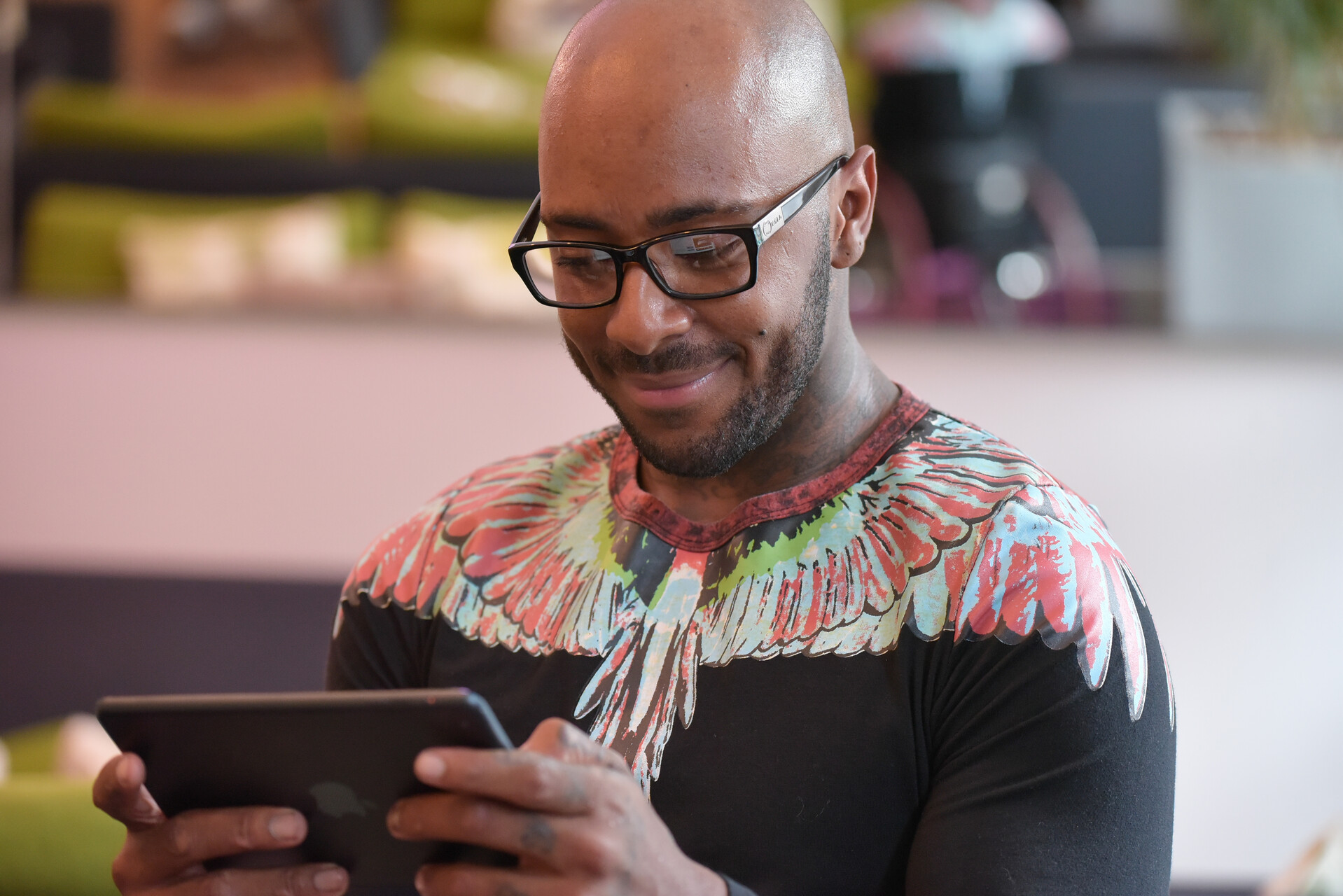 A man with glasses smiling while reading an iPad