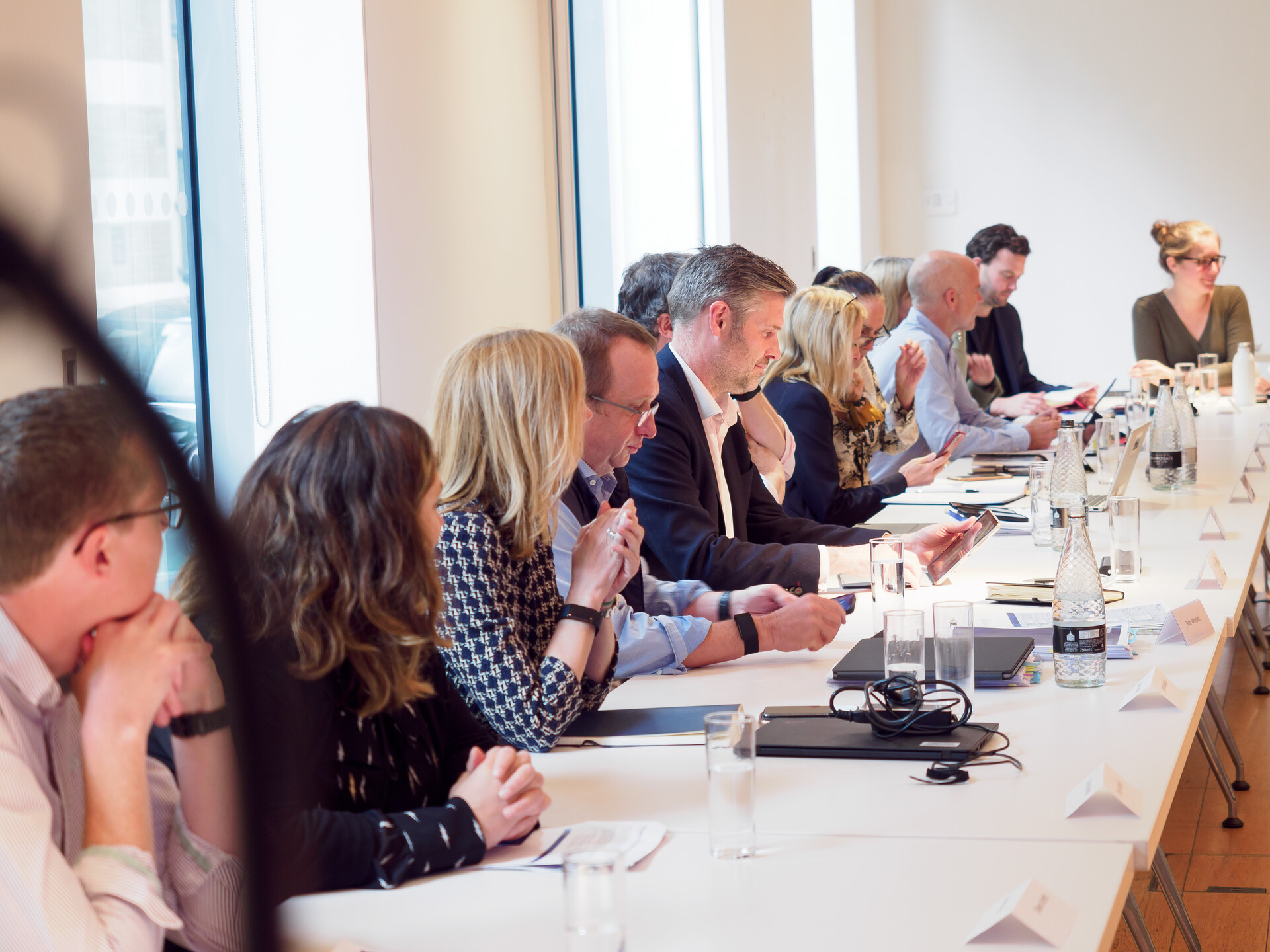 A row of people with name cards in front of them, looking at their phones