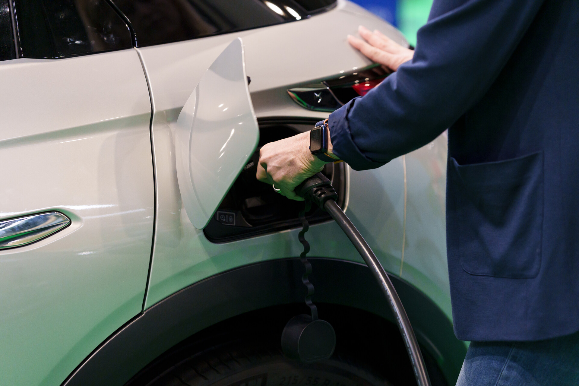 A close-up of a hand plugging a charging socket into an electric car